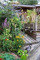 La maison écologique et les terrasses en bois entourées de plantes à fleurs.