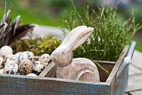 Décoration de Pâques sur une table dans un jardin de printemps. La boîte en bois est remplie d'alto, d'oeufs de caille, d'un lapin de Pâques en bois, de branches de myrtille, de mousse et de plumes.