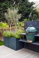 Cuisine extérieure moderne avec barbecue et pots avec Olea europaea 'Oliviers' et Salvia officinalis.