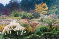 Vue sur jardin avec un étang circulaire central avec fontaine de dragon entouré de plantations luxuriantes de Miscanthus, Cortaderia - Pampas Grass, Calamagrostis et Pennisetum