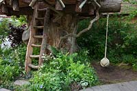 Le RHS Back to Nature Garden, vue de la cabane dans les arbres avec son échelle et sa corde, est planté de fougères, Dryopteris filix-mas et Athyrium filix-femina, Luzula nivea, Lamium et Vinca. RHS Chelsea Flower Show 2019.
