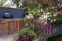 Jardin contemporain de Londres - barbecue sur mesure sur terrasse avec parterre de fleurs surélevé gris. La plantation comprend le smoothie aux baies de Heuchera, la Salvia caradonna, l'Hydrangea anabelle, le Geranium johnsons blue.