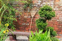 Le râteau en bois s'appuie contre le mur dans un jardin de style japonais, avec des conifères coupés.