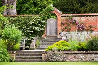 Jardin clos avec marches menant à une porte de jardin en bois, parterres de fleurs environnants dont Allium, rose 'ordre luoise', hydrangea petiolaris.