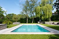 Jardin moderne avec piscine, bord pavé entouré de pelouse