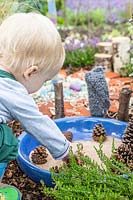 Jeune enfant jouant avec du sable et des pommes de pin dans le jardin sensoriel