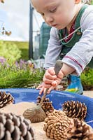 Jeune enfant jouant avec cuillère, sable et pommes de pin dans le jardin sensoriel