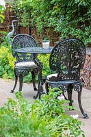 Table et chaises en fer forgé dans le jardin de banlieue avec des paniers de gabion remplis de tuiles et de tuyaux