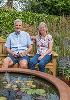 Les propriétaires de jardin se sont assis sur un banc par une pièce d'eau en acier corten