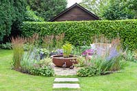 Vue sur jardin de banlieue avec pelouse et parterre de fleurs circulaire avec coin salon pavé et pièce d'eau