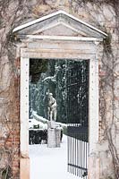 Vue à travers la porte ouverte à la sculpture dans le jardin à la française couvert de neige