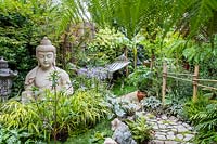 Sculpture de Bouddha dans petit jardin avec plantation exotique
