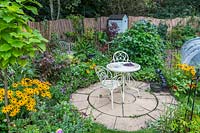 Petite zone pavée circulaire avec des meubles en métal blanc décoré entre fleurs et légumes de style jardin cottage