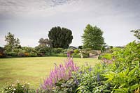 Vue sur la pelouse principale vers des parterres de couleurs luxuriantes plantées, à Bourton House, Gloucestershire, Royaume-Uni.