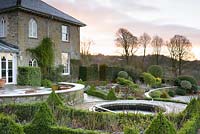Un étang circulaire situé dans une terrasse formelle est entouré de Buxus - Box - couverture et plantation dans un jardin de campagne