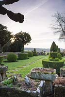 Le jardin topiaire bordé d'auges en pierre, un mur et des urnes, avec campagne au-delà à Rodmarton Manor, Glos, Royaume-Uni.