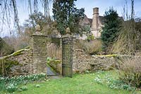 Porte avec fleurons d'ananas au sommet des poteaux de porte, entre le jardin principal et le verger de cerisier à Rodmarton Manor, Glos, Royaume-Uni.