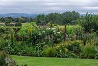 Parterre de fleurs planté de dahlias et de plantes vivaces herbacées dont linaria, helianthus, verbascum et phlox. Au-delà, un aperçu de Blackmore Vale.