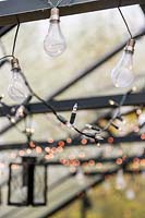 Guirlandes lumineuses et ampoules transparentes suspendues à un toit de serre