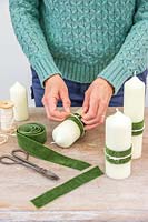 Femme ajoutant un ruban vert de velours décoratif et chaîne crème à la bougie pilier