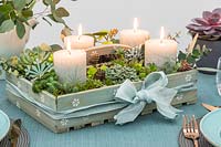 Arrangement de l'Avent dans une boîte en bois avec des bougies pilier sculpté et des plantes succulentes utilisées comme pièce maîtresse sur une table à manger