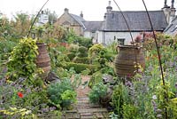 Vue d'ensemble du jardin de cottage avec topiaire, grandes urnes et parterres de fleurs informels.