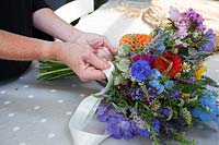 Zelie dans le studio de fleurs fabriquant des bouquets de fleurs noués à la main et fixant avec du raphia et du ruban.
