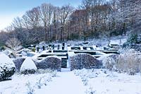 Vue depuis le parterre d'herbes aux jardins de haies couverts de neige et bois en arrière-plan. Haies et colonnes de taxus baccata et haie en forme de vague de Fagus sylvatica au premier plan. Veddw House Garden, Monmouthshire