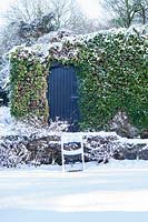 Chaise couverte de neige par garage avec du lierre. Jardin de la maison Veddw