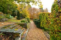 Un chemin de gravier le long de terrasses en pierre couvertes de mousse entouré de Taxus baccata et Fagus sylvatica en automne au jardin de style Arts and Crafts à High Moss, Portinscale, Cumbria
