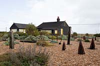 Cottage et jardin sur une plage de galets avec des objets trouvés et des plantes