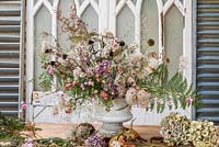 Arrangement floral automnal terminé dans une urne avec des fleurs séchées et fourragées inc échinacée, clématite, fougère, hortensias, échinops