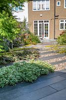Vue sur zone pavée dans le jardin moderne du nord de Londres, avec pavage de schiste Ebony Cloud avec galets polis japonais.