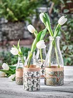 Tulipes dans des vases de bouteilles de lait enveloppées de papiers décoratifs.
