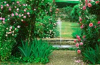 Fontaine à eau dans l'étang dans le jardin à la française avec des roses en fleurs.