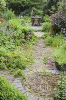 Un motif circulaire de pierres incrustées à la jonction de chemins dans un jardin de cottage en juin entouré d'aquilegias auto-ensemencées et de fraises des bois.