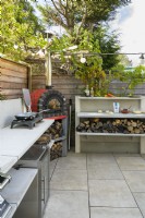Cuisine extérieure avec four à pizza rouge et plaque de cuisson avec rangement en bois intégré dans un petit jardin familial moderne