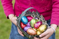 Enfant tenant un panier avec des œufs en chocolat colorés à Pâques