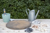 Tremplin circulaire, arrosoir, pot de coulis en poudre, grattoir, chiffon et divers tas de pierres disposés sur une table