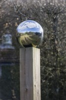 Globe en acier inoxydable reflétant le jardin environnant. monté sur colonne en bois. Février. Printemps