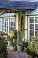 Porche et véranda peints en vert avec rouleau de jardin ancien et plantation de pots de printemps.