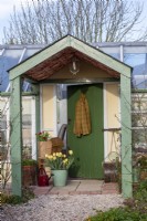 Porche peint en vert avec rouleau de jardin ancien et pots plantés au printemps