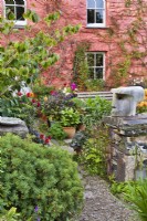 Mur bas en pierre avec sculpture en bois dans un chalet avant jardin plein de plantes.