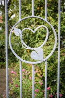 Détail d'un coeur et de feuilles sur grille métallique à l'entrée du jardin.