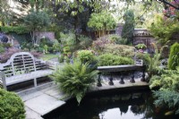 Jardin clos avec parterres mixtes avec plantation de conifères, fougères, Acer, Phyllostachys et Azalée. Coin salon près de l'étang