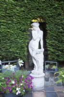 Statue de jardin classique encadrée par une haie de conifères taillée