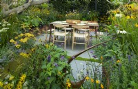 Une salle à manger sur une terrasse pavée entourée de plantations d'automne dans des pots en bois dans le Parsley Box Garden, un jardin sanctuaire comestible.