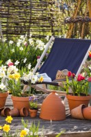 Des pots de fleurs printanières et une chaise longue en bois sur un patio.
