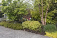 Des couches d'arbres à feuilles caduques et à feuilles persistantes, d'arbustes et de plantes vivaces filtrent la vue du coin salon privé dans le jardin de devant