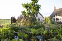 Vue sur un étang de jardin avec des chaumières au-delà